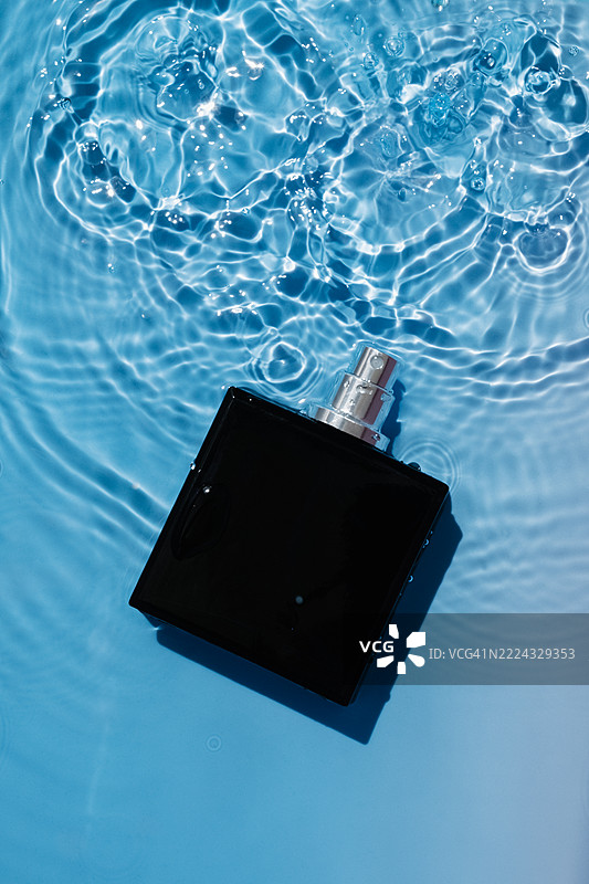黑色香水瓶漂浮在夏日阳光下的游泳池水面上图片素材