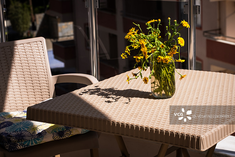 阳光下的露台桌上摆放着一瓶黄色花卉图片素材