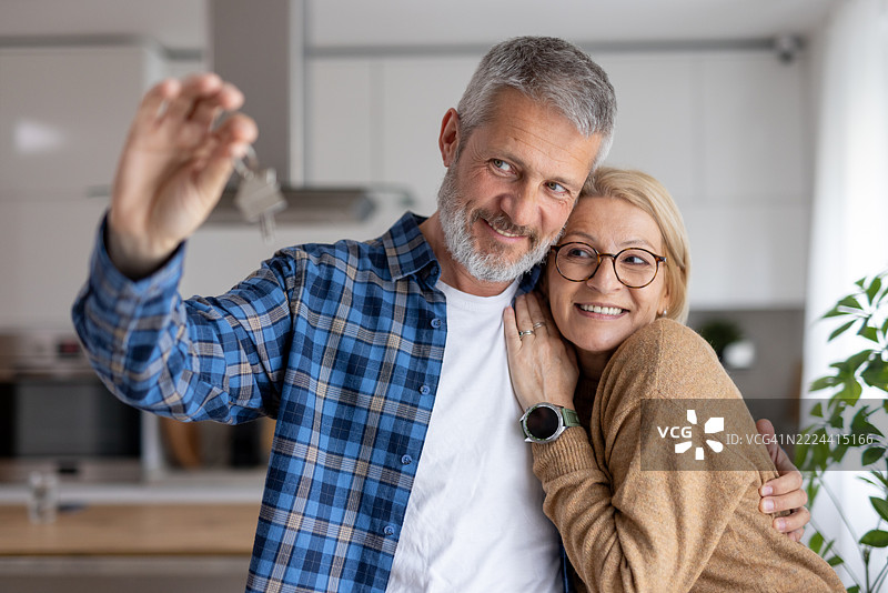 幸福的情侣在温馨的现代厨房中握着钥匙。图片素材