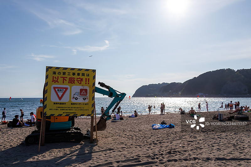 海滩维护的重型设备。逗子海滩挤满了来自海外的游客。地平线上是江之岛和山的轮廓。这里也是风帆冲浪和立式划水的圣地。一些人在防波堤上钓鱼。图片素材