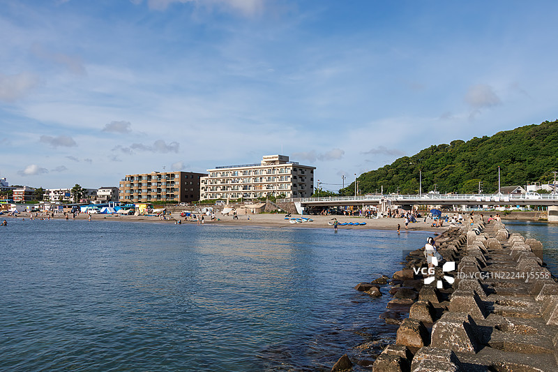 逗子海滩挤满了来自海外的游客。地平线上是江之岛和山的轮廓。这里也是风帆冲浪和立式划水的圣地。一些人在防波堤上钓鱼。图片素材