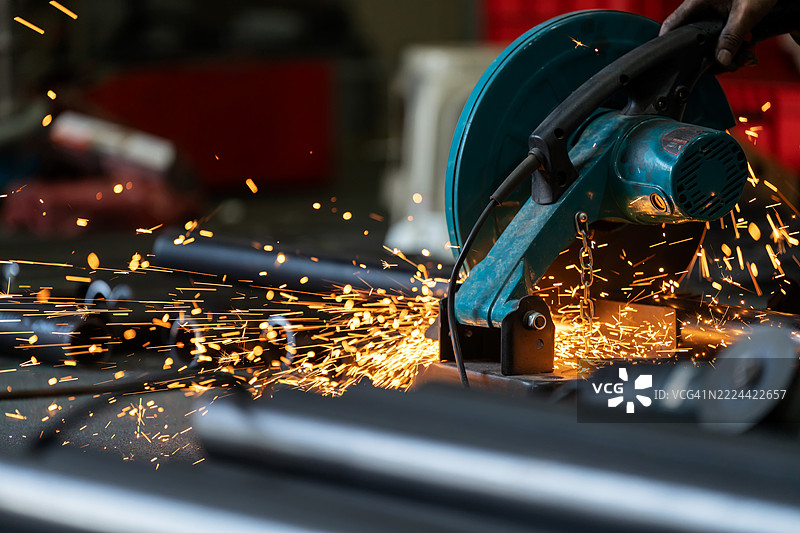 一位熟练工程师正在使用工业级工具进行精确的金属切割特写。火花以节奏感的方式迸发，展示了在先进磨削技术中所需的精细和控制，精准与视觉冲击相结合。图片素材