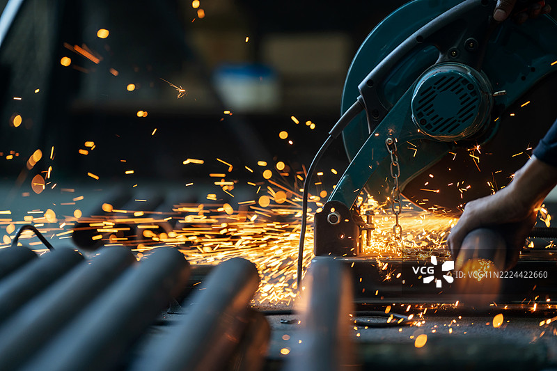 穿着阻燃服和安全面罩的技术人员在受控的工业环境中磨削金属。火花照亮了现场，展现了机械的力量和工作场所保护的重要性。图片素材