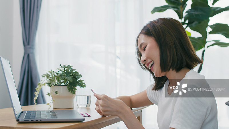 年轻亚洲女性在家用笔记本电脑研究医学以促进健康与福祉。图片素材