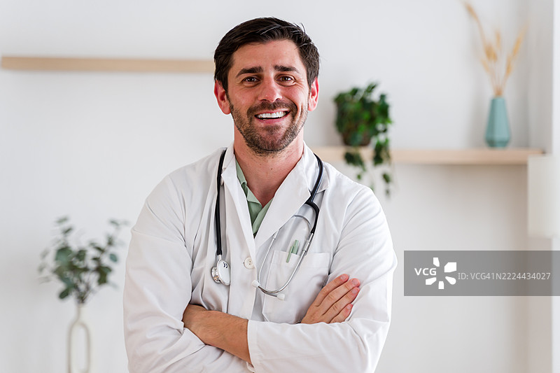 微笑的医生交叉双臂，佩戴听诊器的肖像图片素材