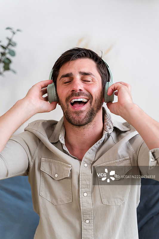 年轻男子戴着耳机享受音乐并唱歌图片素材