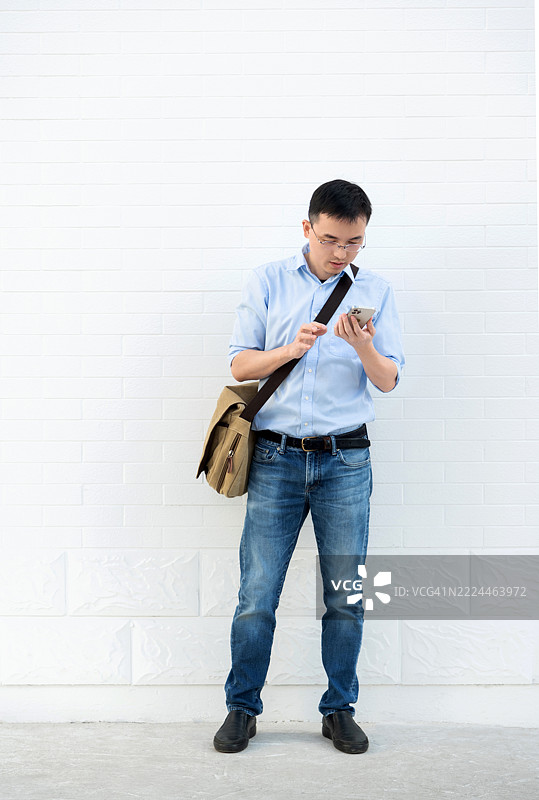 年轻男子背着肩包，正在使用智能手机图片素材