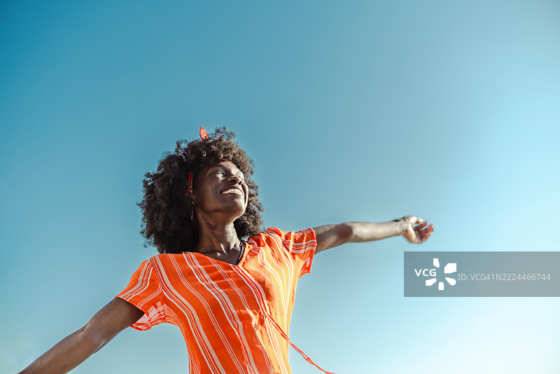穿着橙色衬衫的快乐女性享受着开阔的蓝天图片素材