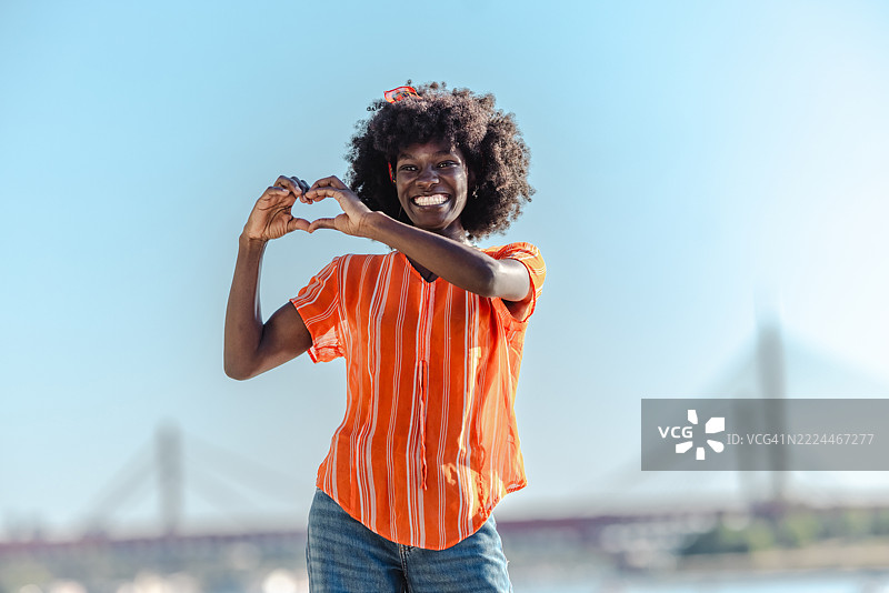 微笑的女性在风景如画的城市景观旁做出心形手势图片素材