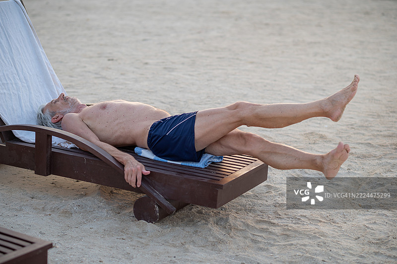 阳光下的沙滩躺椅上锻炼的老年男子图片素材