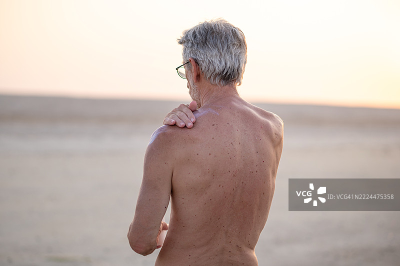 男人在开阔的风景中日落时给肩膀涂防晒霜图片素材