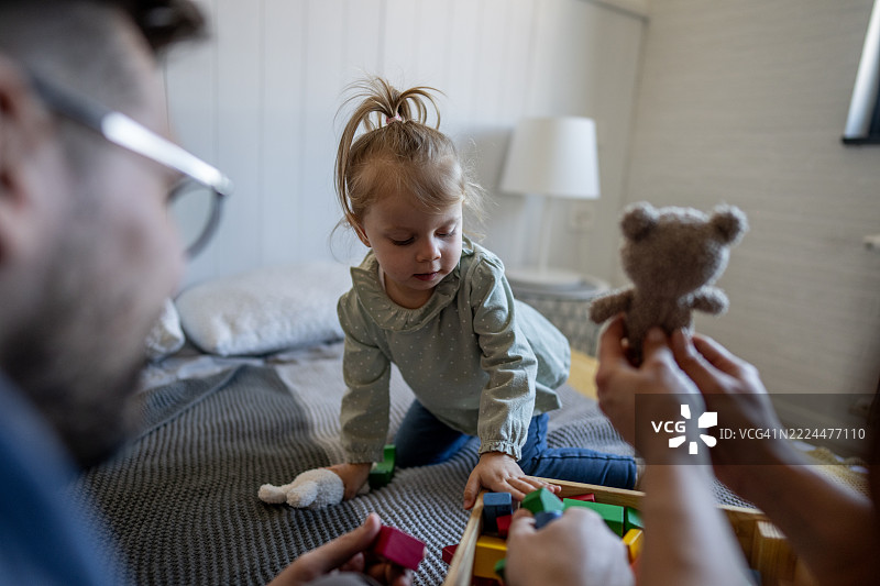 父母与女儿在床上玩积木和泰迪熊图片素材