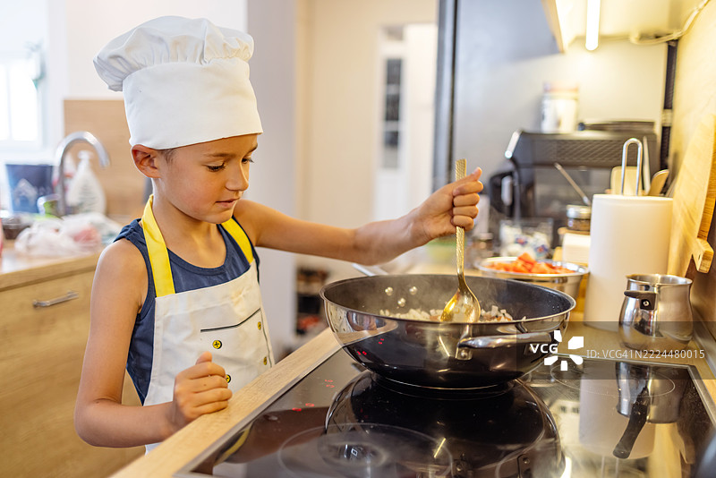 年轻厨师在现代厨房中穿着围裙和厨师帽烹饪图片素材