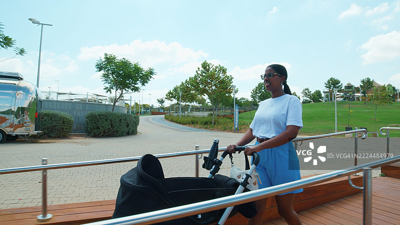 年轻人在阳光明媚的公园推婴儿车图片素材
