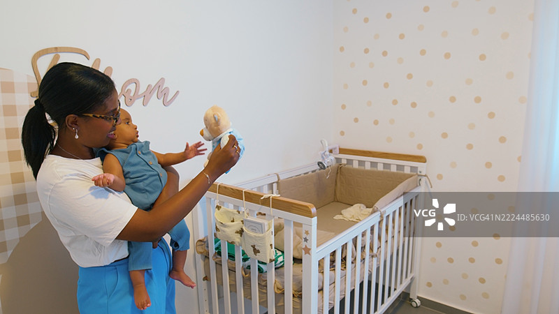 母亲在婴儿房里用泰迪熊逗乐她的男婴图片素材