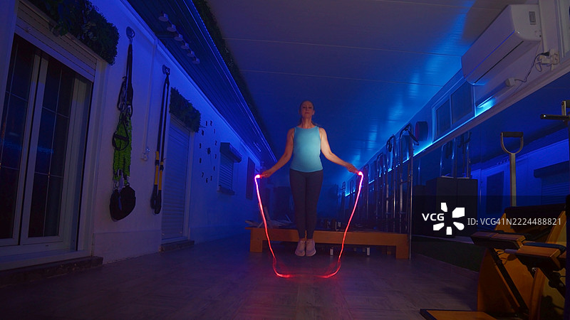在健身房里，女人在霓虹灯下跳绳图片素材