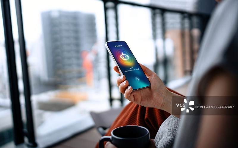 年轻的亚洲女性在阳台上放松，正在与智能手机上的虚拟助手ChatGPT AI聊天应用交谈。背景是城市风景。聊天机器人对话。日常生活中的AI服务。互联网虚拟助手。人们、人工智能、创新与科技。图片素材