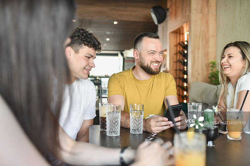 男人在手机上给朋友们展示有趣的宠物视频，朋友们都在笑着。图片素材