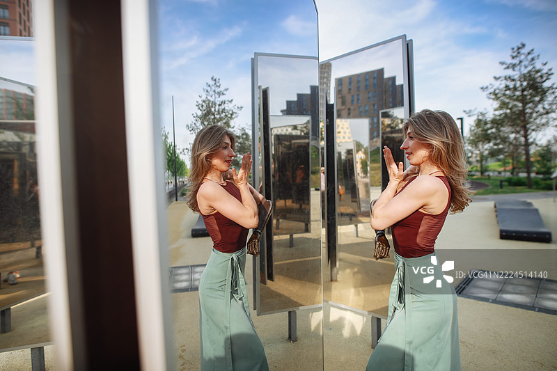 美丽苗条的女性穿着裙子在夏季城市公园的镜子前排练舞蹈，自信满满，享受生活中真实快乐的时刻。图片素材