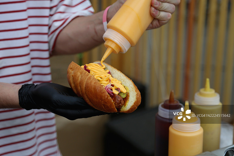 厨师的手在户外小吃摊制作热狗，配有香肠、红洋葱、腌黄瓜和芥末酱。图片素材