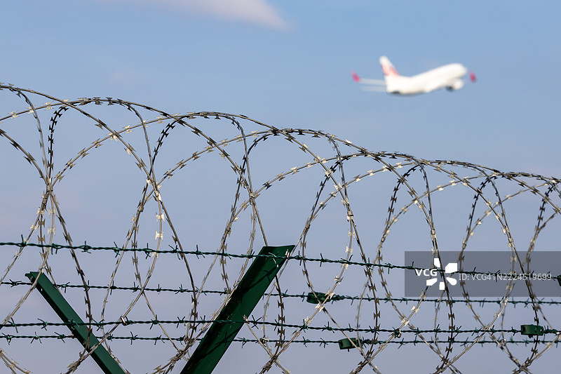 带刺铁丝网与空中飞行的客机图片素材