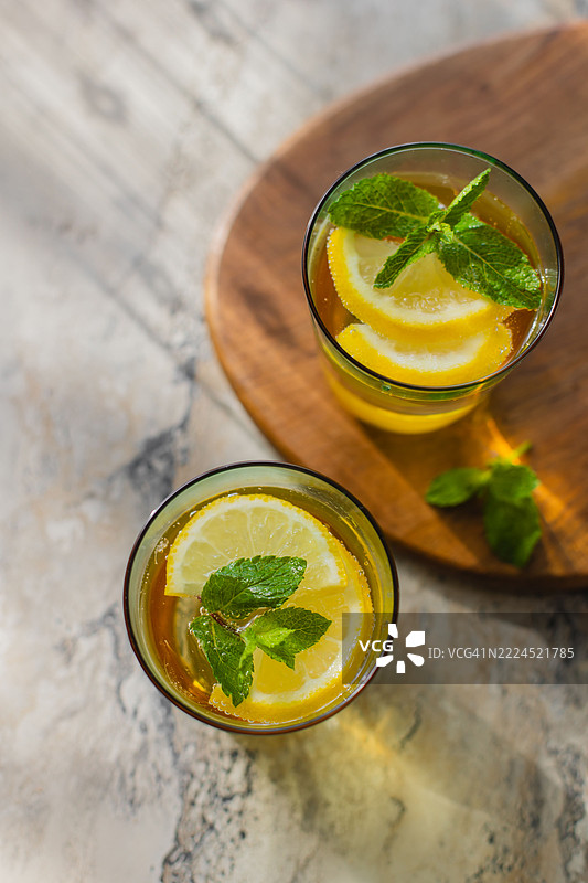 生动的夏季饮品描绘，配有柠檬片和薄荷叶，摆放在大理石上。图片素材