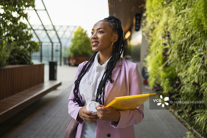 年轻经理在现代办公室里走动，手里拿着咖啡和文件。图片素材