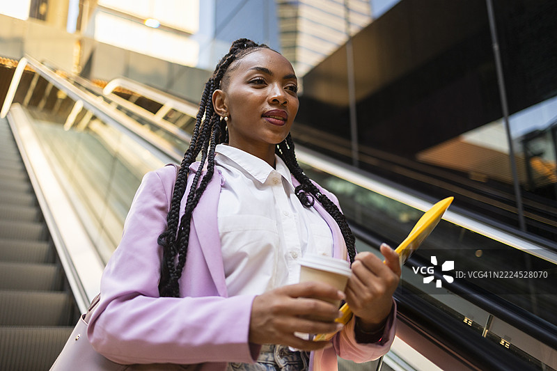 年轻女商人手拿咖啡和平板电梯上行图片素材