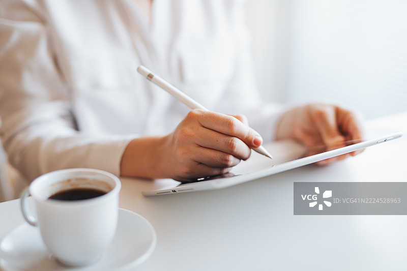 在咖啡桌上，手部特写使用带触控笔的平板电脑。图片素材