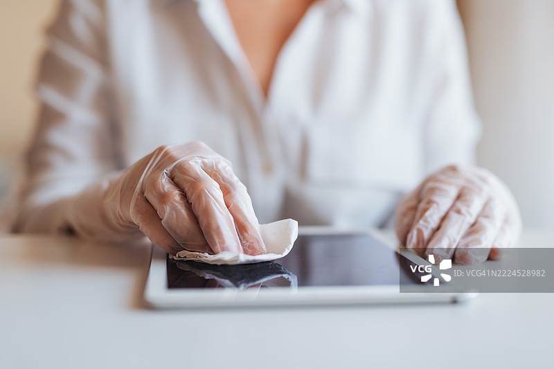 戴着手套的人用湿巾消毒平板电脑图片素材