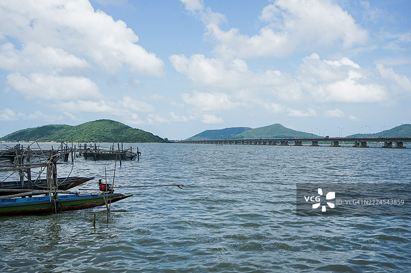 长尾船漂浮在海岸，背景是长长的混凝土桥和山脉，泰国宋卡。图片素材