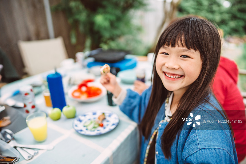 微笑的年轻女孩在后院花园享受户外家庭聚餐图片素材