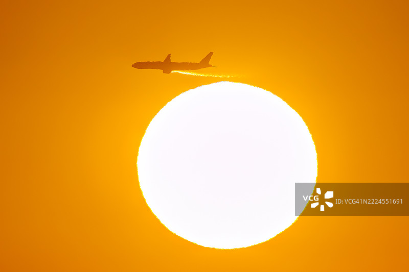 第一缕阳光与一架客机和鸟的剪影。它即将降落在附近的羽田机场。第一缕阳光从运河对岸的烟囱和电厂、钢铁厂上升。图片素材