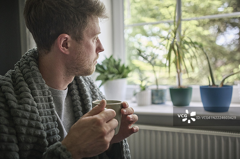 严肃的男人手持咖啡杯透过窗户凝视图片素材