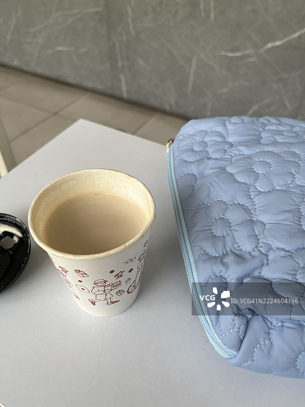 白色桌子上放着纸杯咖啡，旁边是蓝色绗缝袋。图片素材