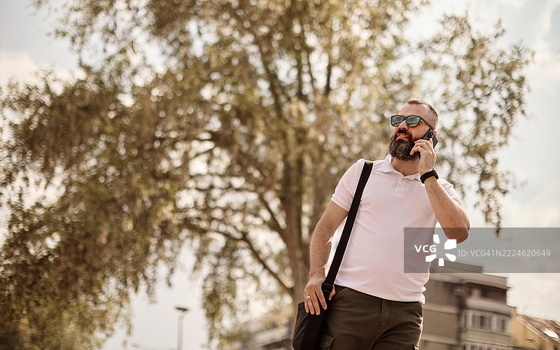 一位年轻帅气的有胡子的男人在走路时打电话。图片素材