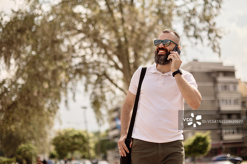 一位年轻帅气的有胡子的男人在走路时打电话。图片素材