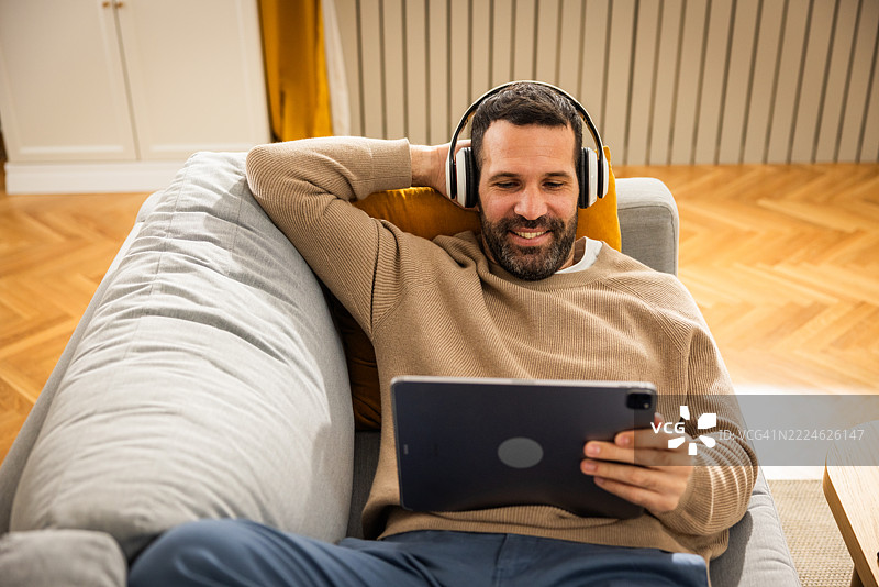 男人躺在沙发上，用数字平板观看电影图片素材