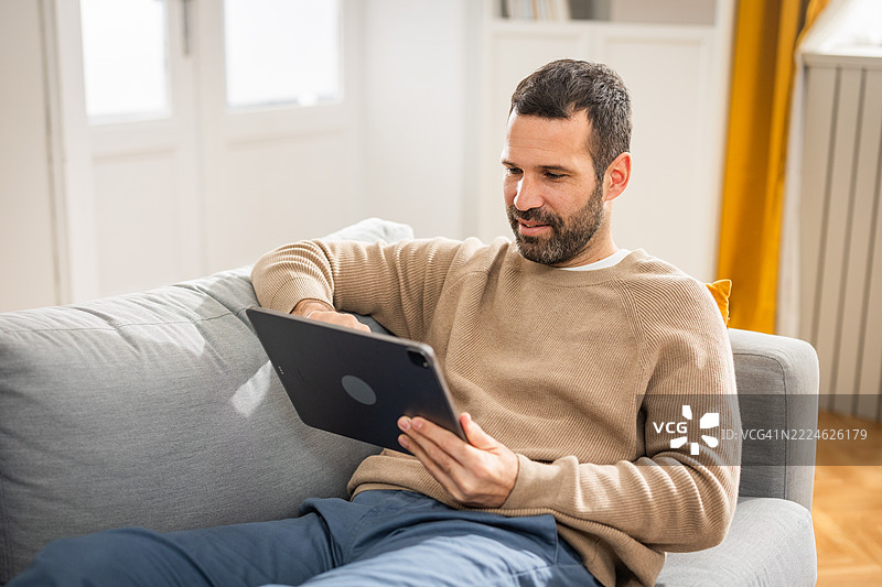 男人躺在沙发上，用数字平板观看电影图片素材
