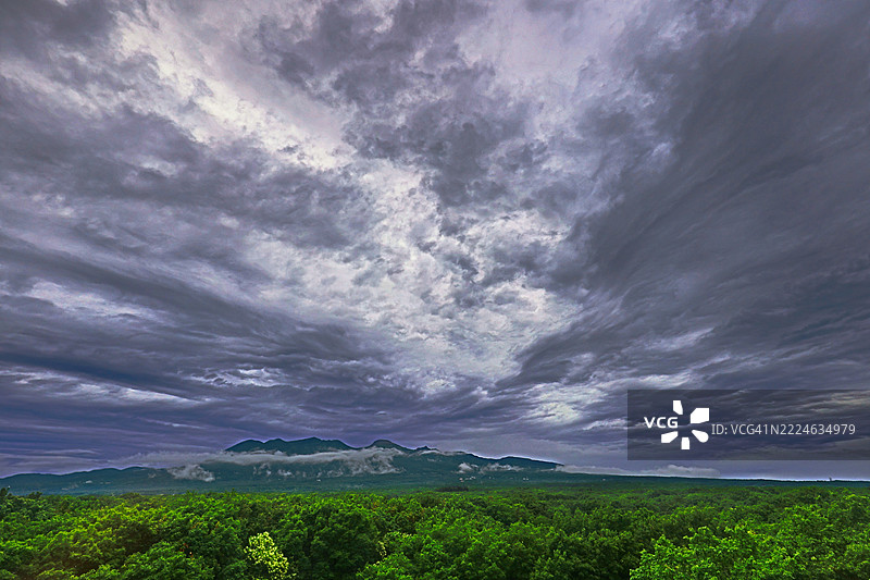 戏剧性的天空笼罩在郁郁葱葱的绿色山脉上，暗示着一场即将来临的风暴或其余波。图片素材