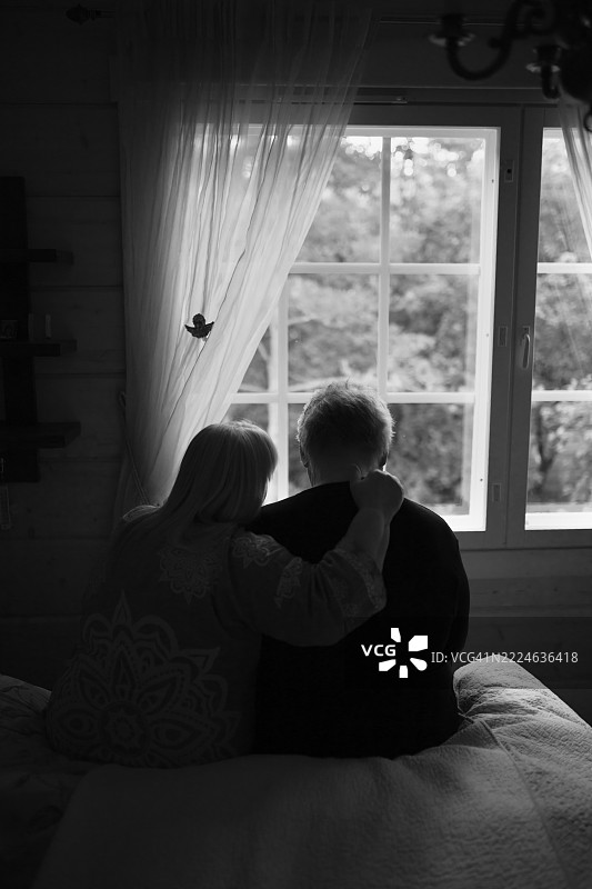 一位悲伤的老年男子坐在床上，与他的妻子在一起，成熟的夫妻在家中，田园风格的木屋图片素材