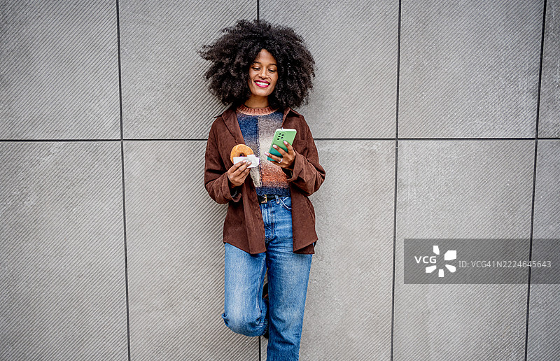 年轻女性在城市中享受甜甜圈并浏览智能手机图片素材