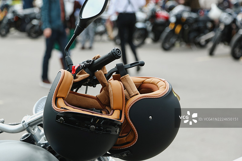 两个复古摩托车头盔放在摩托车把手上，背景是模糊的城市街道。图片素材