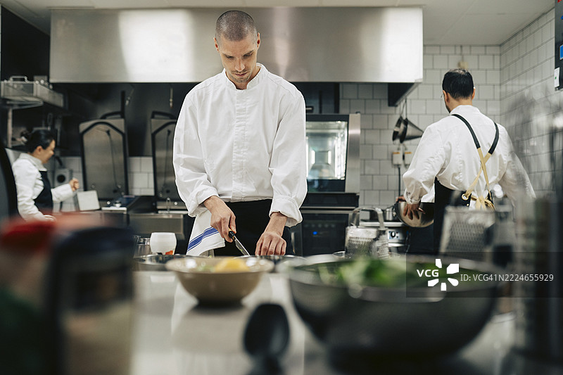 穿着制服的男厨师在餐厅的厨房台面上切菜图片素材