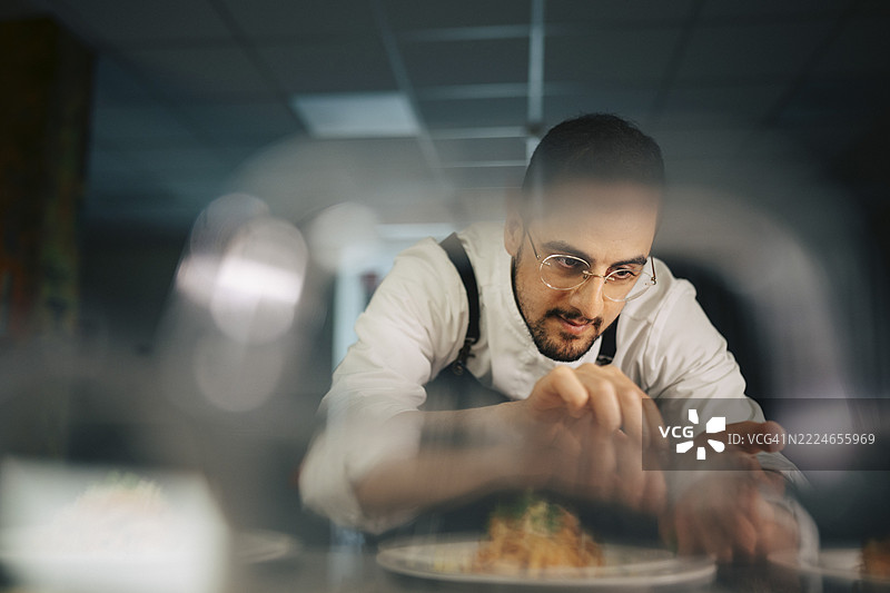 专注的男性厨师在餐厅厨房为菜肴装饰配料图片素材