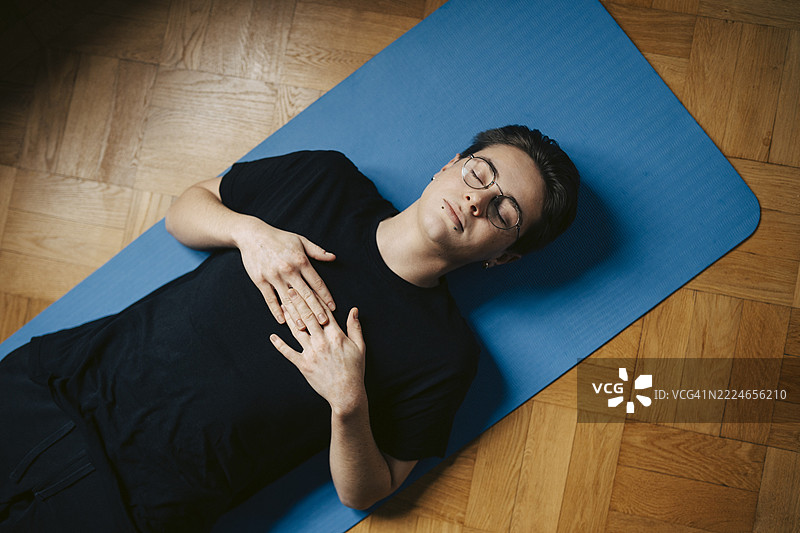 高角度视图的无忧无虑的年轻男子躺在家中的健身垫上，闭着眼睛。图片素材