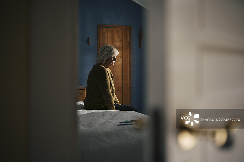 伤心的老年女性坐在家中卧室的床上图片素材