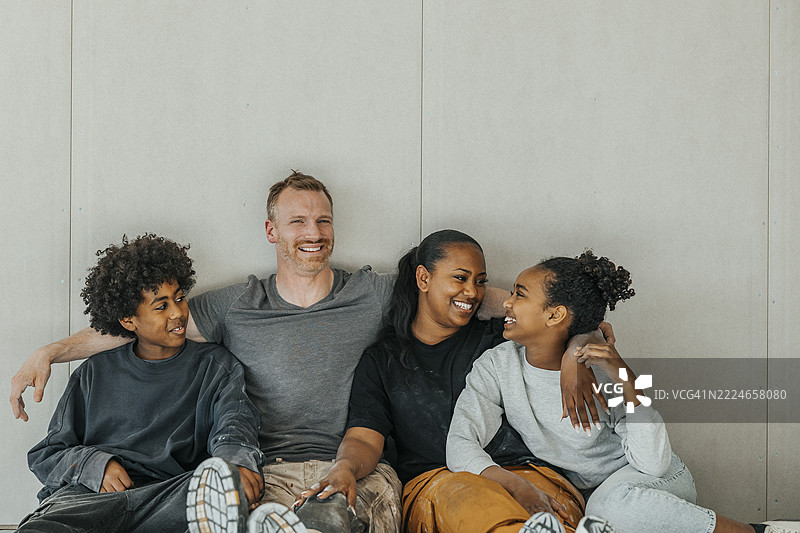 微笑的多种族家庭在房屋施工现场的墙边悠闲地坐着图片素材