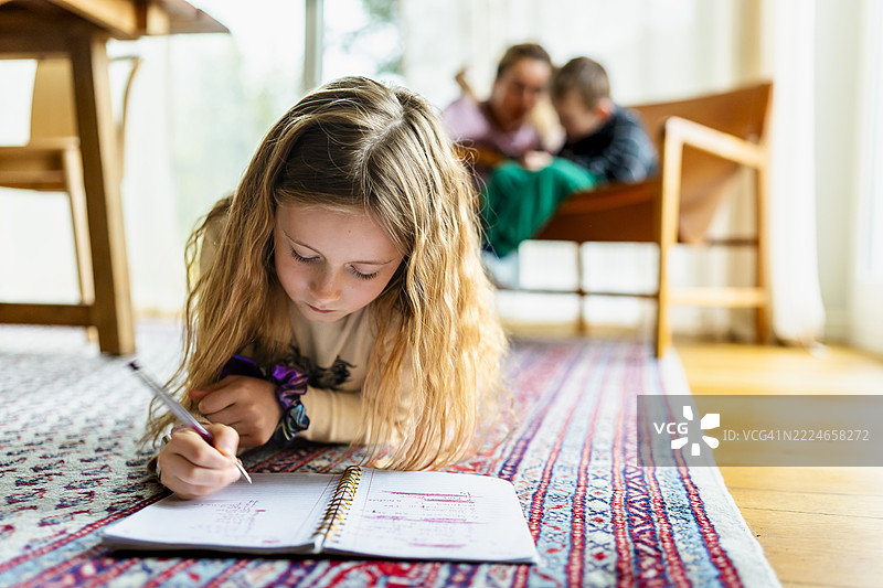 金发女孩躺在地毯上做作业图片素材