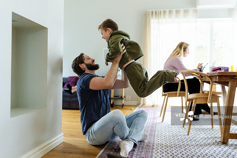 父亲在家里盘腿坐在地上与儿子玩耍图片素材